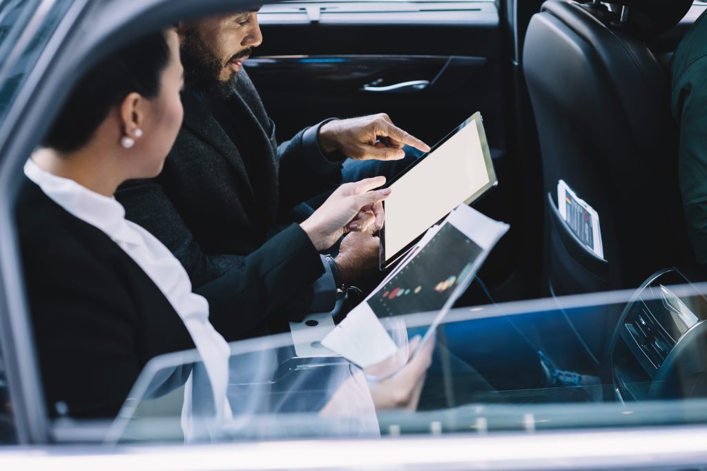 tranquil multiracial colleagues with papers interacting with digital tablet with blank screen while discussing done work in car